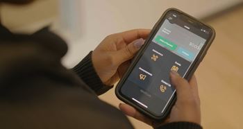 A person is holding a phone with a dark interface and a gold-colored app icon visible.at Skyway Apartments, Calgary